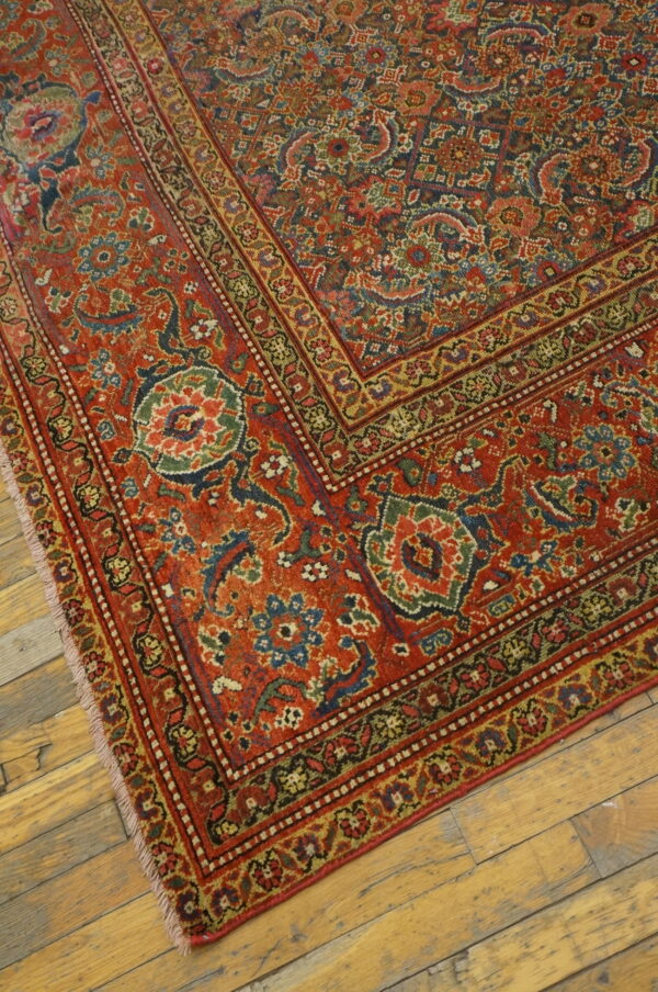 Ornate red and blue patterned rug with complex borders lying diagonally on rustic hardwood floors.