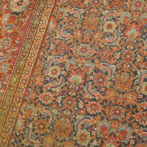 Traditional rug with dense floral patterns in deep red, navy, blue, and green resting on wood planks.