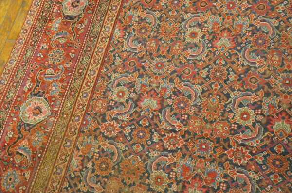 Traditional rug with dense floral patterns in deep red, navy, blue, and green resting on wood planks.