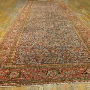 A very long, low-pile runner rug with a dense traditional blue and rust pattern rests on light wood floors.