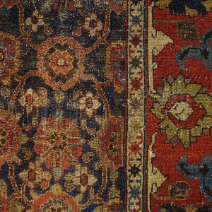 Detailed low-pile rug featuring a traditional floral pattern in navy, rust, and gold on wood flooring.