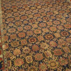 A low-pile rug featuring a dense floral pattern in red, gold, and green on a navy field, bordering wood planks.