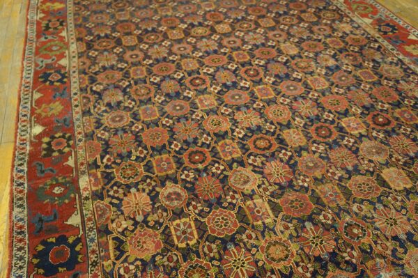 A low-pile rug featuring a dense floral pattern in red, gold, and green on a navy field, bordering wood planks.