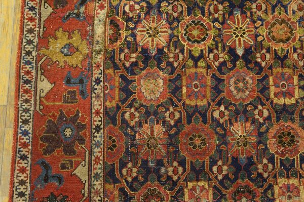 Close-up of a low-pile rug with navy, red, green, and gold floral patterns resting on light wood planks.