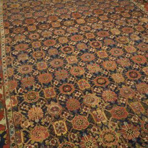 Navy rug with repeating geometric floral motifs in rust, gold, and green on light wood flooring.