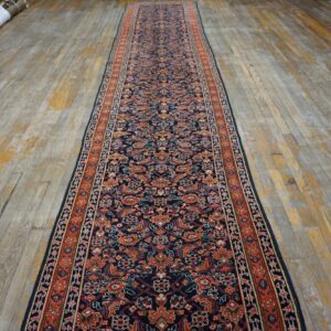 Navy blue traditional runner rug with orange and cream floral patterns placed on distressed wood floorboards.