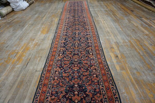 Navy blue traditional runner rug with orange and cream floral patterns placed on distressed wood floorboards.