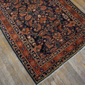Low-pile navy rug with dense orange and blue traditional patterns on distressed wood flooring.