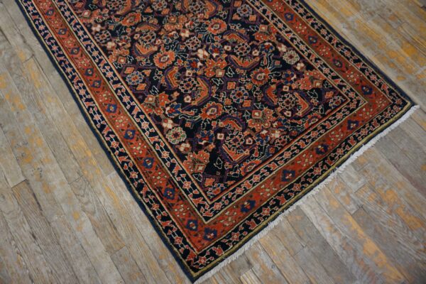 Low-pile navy rug with dense orange and blue traditional patterns on distressed wood flooring.