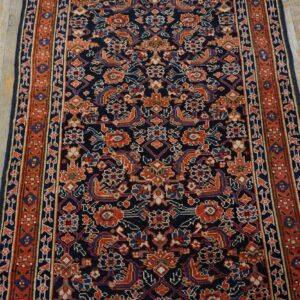 Intricate navy, red, and blue patterned runner rug on light, aged wood floorboards.