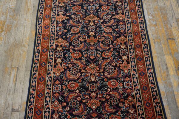 Intricate navy, red, and blue patterned runner rug on light, aged wood floorboards.