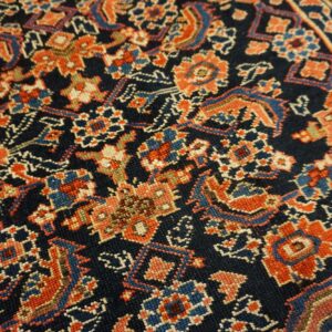 A dense, low-pile rug featuring intricate floral patterns in orange, blue, and cream on a dark navy ground.
