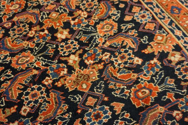 A dense, low-pile rug featuring intricate floral patterns in orange, blue, and cream on a dark navy ground.