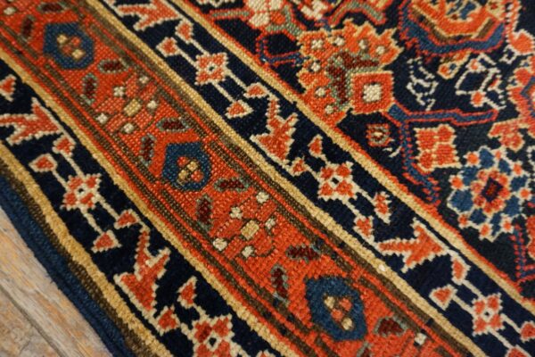 Detail of a low-pile traditional rug border in navy, rust, and tan colors over light wood flooring.