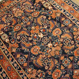 Low-pile navy rug with intricate orange and blue traditional patterns, visible against rustic light wood flooring.