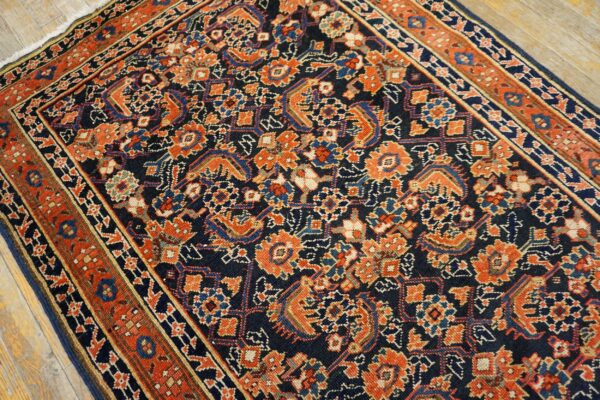 Low-pile navy rug with intricate orange and blue traditional patterns, visible against rustic light wood flooring.