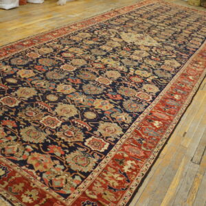 Navy and rust floral rug with a low pile, displayed on worn, light wood plank flooring.