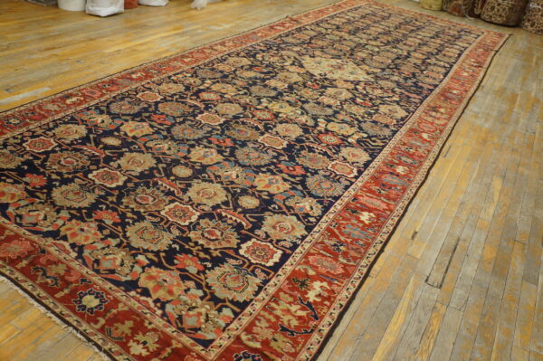 Navy and rust floral rug with a low pile, displayed on worn, light wood plank flooring.