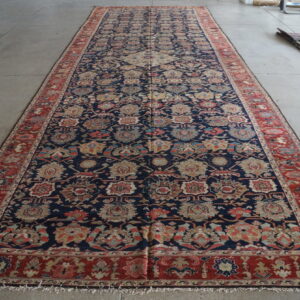 Dark blue runner rug with multi-colored floral designs and a red border lying on a gray floor.