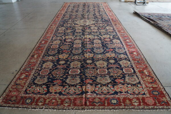 Dark blue runner rug with multi-colored floral designs and a red border lying on a gray floor.