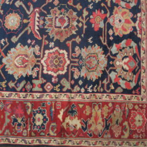 An intricate, colorful rug detail featuring a navy blue field with stylized flowers and a wide red geometric border.