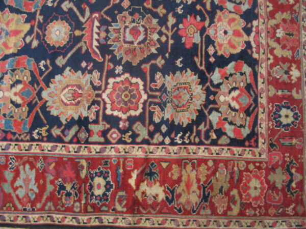 An intricate, colorful rug detail featuring a navy blue field with stylized flowers and a wide red geometric border.