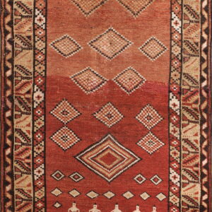 Red and tan runner rug featuring abrash, geometric diamonds, and rows of stylized figures within the field.