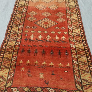 Geometric runner rug with a red and tan field showing abstract figures and diamond patterns on grey fabric.