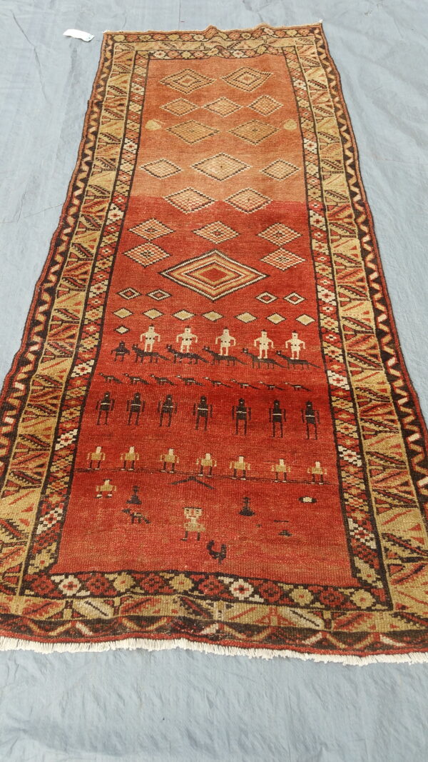 Geometric runner rug with a red and tan field showing abstract figures and diamond patterns on grey fabric.