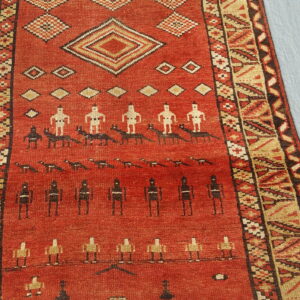 Red rug with figural and geometric patterns in tan, black, and white, resting on a light blue surface.