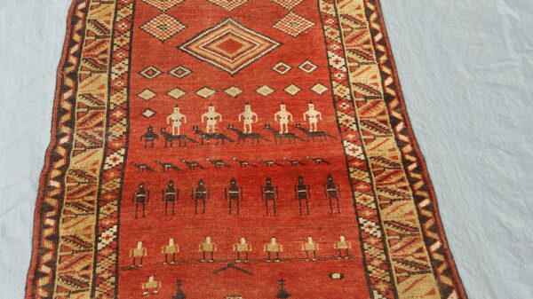 Red rug with figural and geometric patterns in tan, black, and white, resting on a light blue surface.
