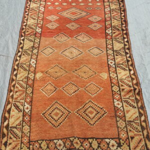 Geometric runner rug in rust and beige with stacked diamond designs lying on a wrinkled gray-blue surface.