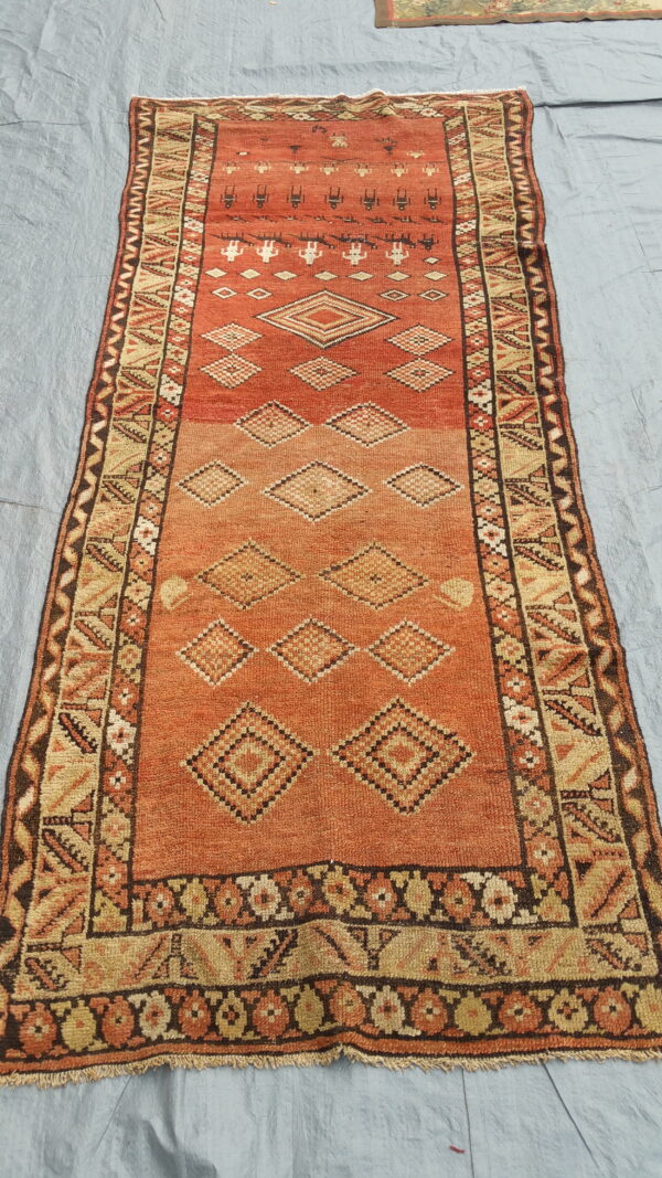 Geometric runner rug in rust and beige with stacked diamond designs lying on a wrinkled gray-blue surface.