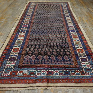 A dark blue runner rug with intricate patterns and multi-colored borders lies on worn wood flooring.