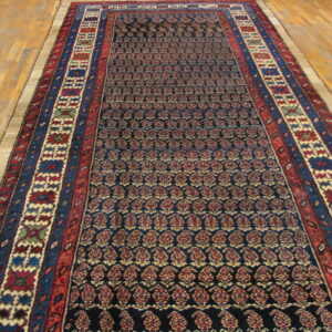 Low-pile runner rug with a dark blue repeating paisley field and wide red and blue geometric borders.
