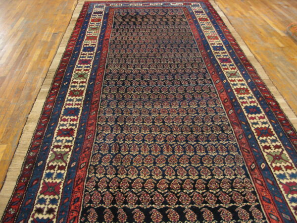 Low-pile runner rug with a dark blue repeating paisley field and wide red and blue geometric borders.