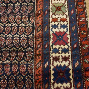 Dark patterned rug showing multi-colored paisley field and geometric borders on light wooden planks.