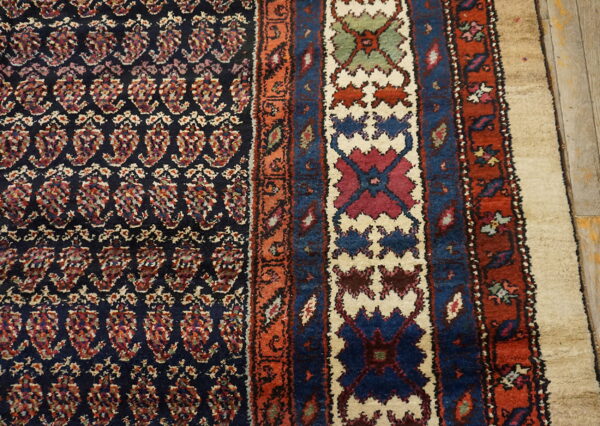 Dark patterned rug showing multi-colored paisley field and geometric borders on light wooden planks.