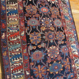Dark blue rug with floral patterns and a border of stylized animal figures rests on wood plank flooring.