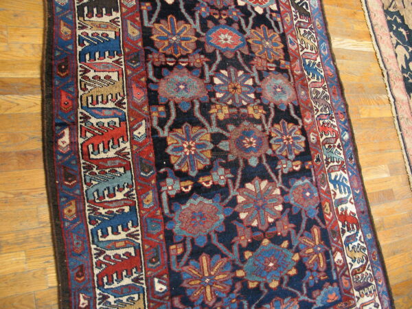 Dark blue rug with floral patterns and a border of stylized animal figures rests on wood plank flooring.