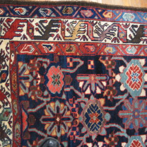 Traditional rug corner in navy, red, and cream with stylized bird and floral patterns on hardwood.