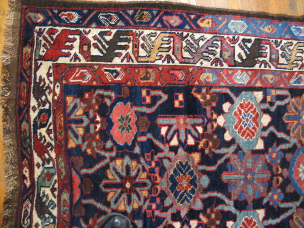 Traditional rug corner in navy, red, and cream with stylized bird and floral patterns on hardwood.