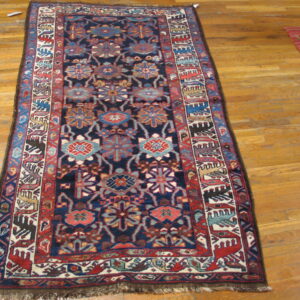 Narrow rug with a dense geometric pattern in navy, red, teal, and cream on natural wood flooring.