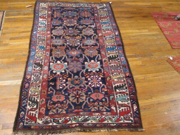 Narrow rug with a dense geometric pattern in navy, red, teal, and cream on natural wood flooring.