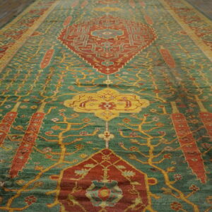 Ornate teal rug featuring rust red medallions and intricate yellow tree patterns on dark wood flooring.