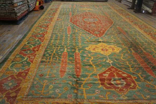Textured green rug featuring rust red medallions and yellow designs on worn wood flooring.