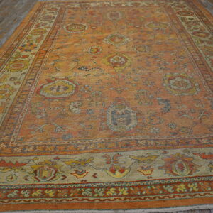 Distressed orange traditional rug with multi-color floral patterns and a wide border on rustic wood planks.