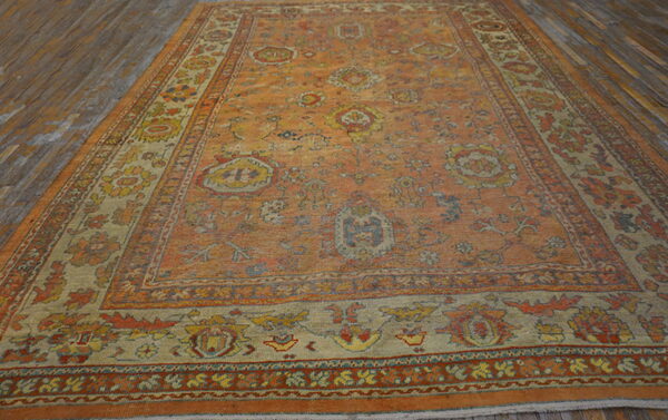 Distressed orange traditional rug with multi-color floral patterns and a wide border on rustic wood planks.