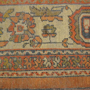 Woven rug detail showing a border of rust, cream, and blue geometric and stylized floral designs.