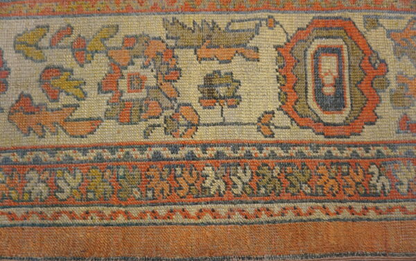 Woven rug detail showing a border of rust, cream, and blue geometric and stylized floral designs.